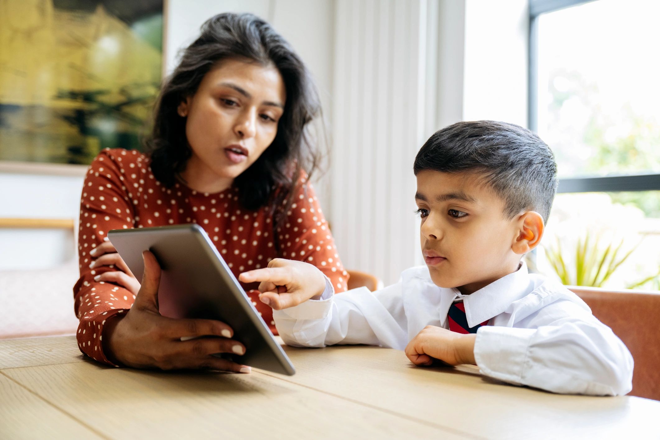Mother assisting schoolboy with homework on portable device