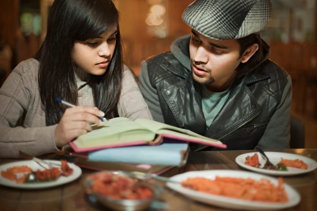 College student friends learning and teaching together in a restaurant.